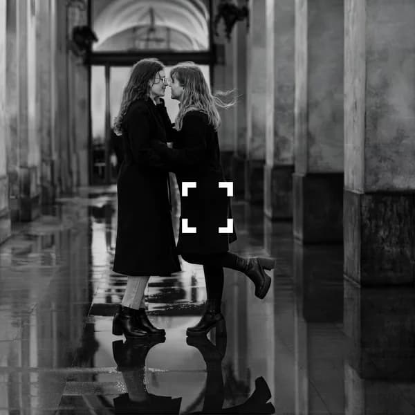 Couple enlacé sous des arcades, reflets au sol, en noir et blanc