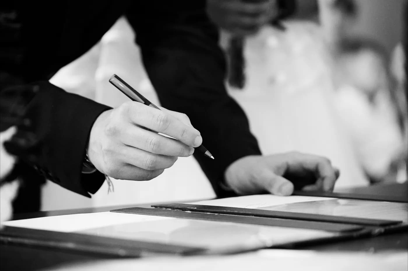 Signature des registres, cadrage serré sur les mains, en noir et blanc